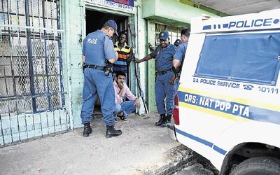 Nazil Munssi, surrounded by police, in front of his looted shop on Friday. Townships including Soweto have been hit by looters targeting foreign-owned stores. Picture: AFP/STEFAN HEUNIS