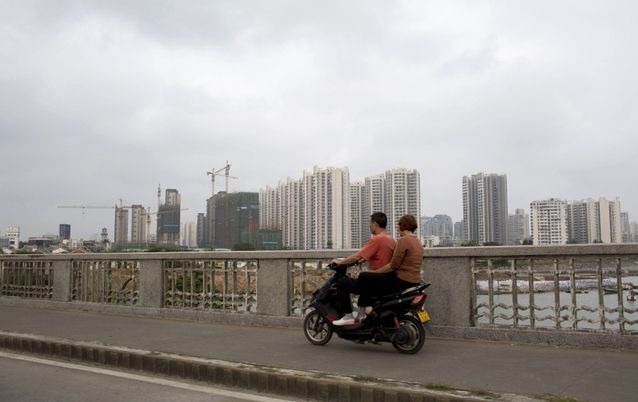 A couple on a scooter ride past construction projects and completed apartment buildings in Haikou, Hainan province, China. Picture: BLOOMBERG