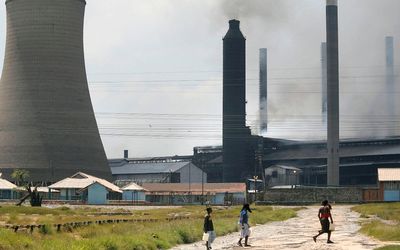 Residents walk down a road in front of a plant owned by Mopani Copper Mines Plc in Kitwe, a town on the Copperbelt in northern Zambia.  Picture: BLOOMBERG/JEAN-CLAUDE COUTAUSSE