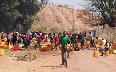 SURVIVING:  People fetch water outside  a mine run by Sicomines in Kolwezi, Congo. Work is tailing off as Glencore has suspended operations at its Katanga copper mine. Picture: REUTERS/AARON ROSS