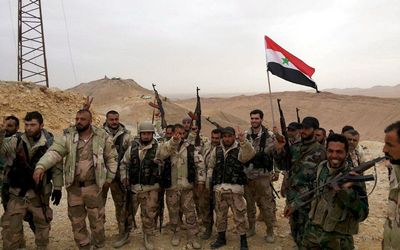 Forces loyal to Syria's President Bashar al-Assad flash victory signs and carry a Syrian national flag on the edge of the historic city of Palmyra in Homs Governorate on Saturday. Picture: REUTERS