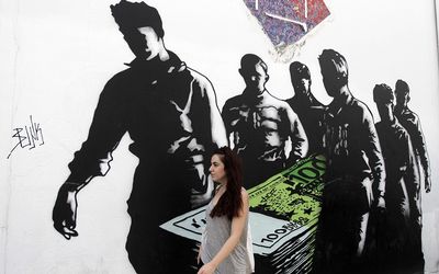 A woman walks past a graffiti titled 'Death of Euros', in Athens, Greece, on Tuesday. Picture: EPA/ORESTIS PANAGIOTOU